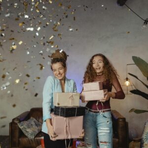Two women rejoicing amidst confetti with gift boxes in a cheerful indoor setting.
