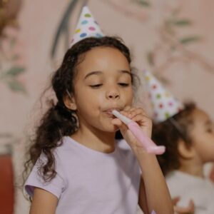 Two young girls in party hats enjoying a birthday party indoors.